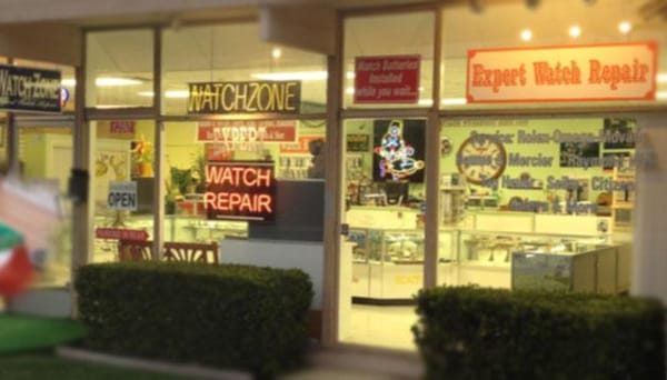 The Watch Zone storefront at dusk, with neon Watch Zone and Watch Repair signs and an Expert Watch Repair banner